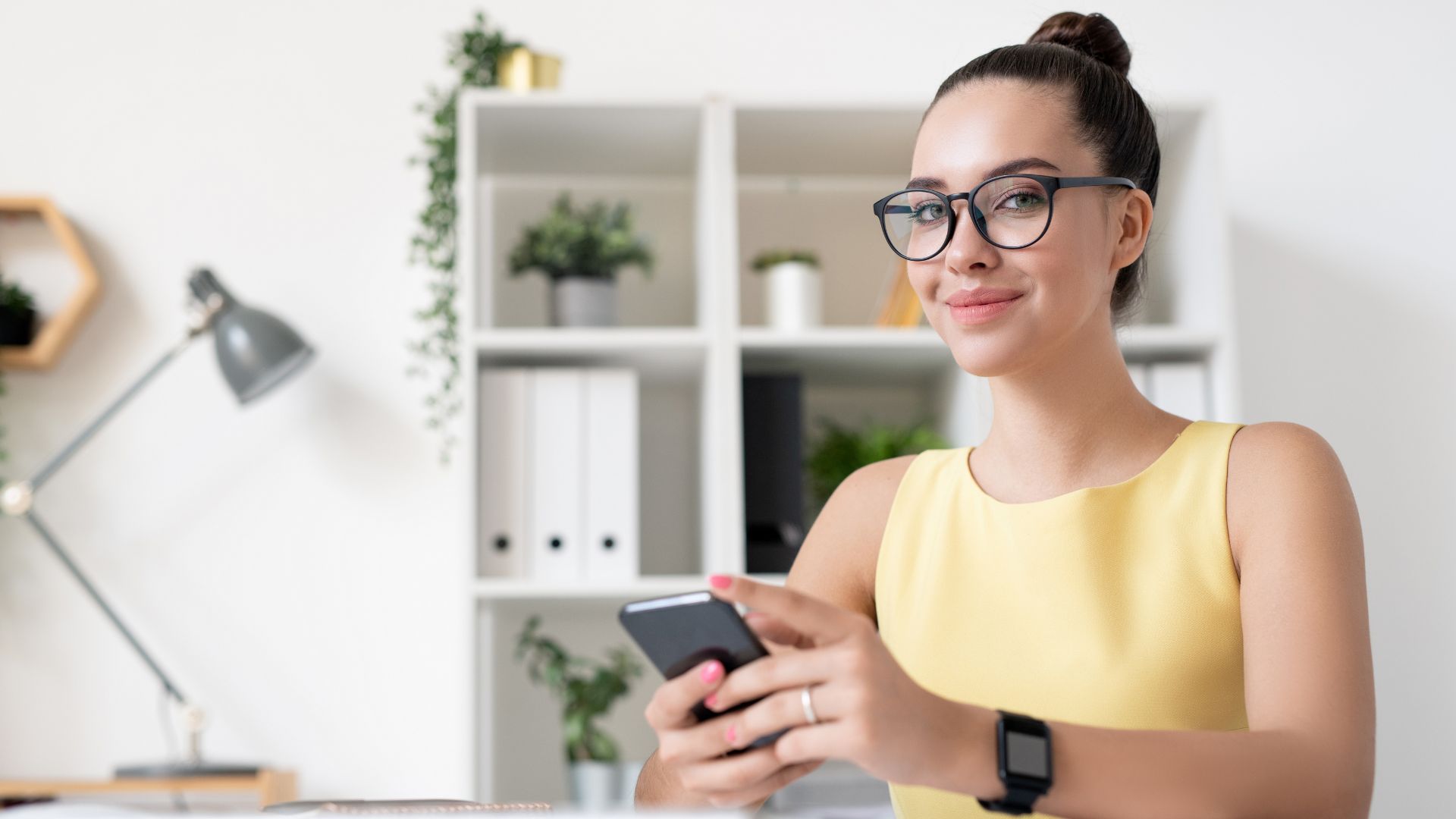 Local SEO, Professional Woman with Smartphone in Modern Office Setting - Local SEO and Web Design Specialist in Yellow Sleeveless Top, Glasses, and Home Decor Enhanced Ambiance Web Design, East Texas